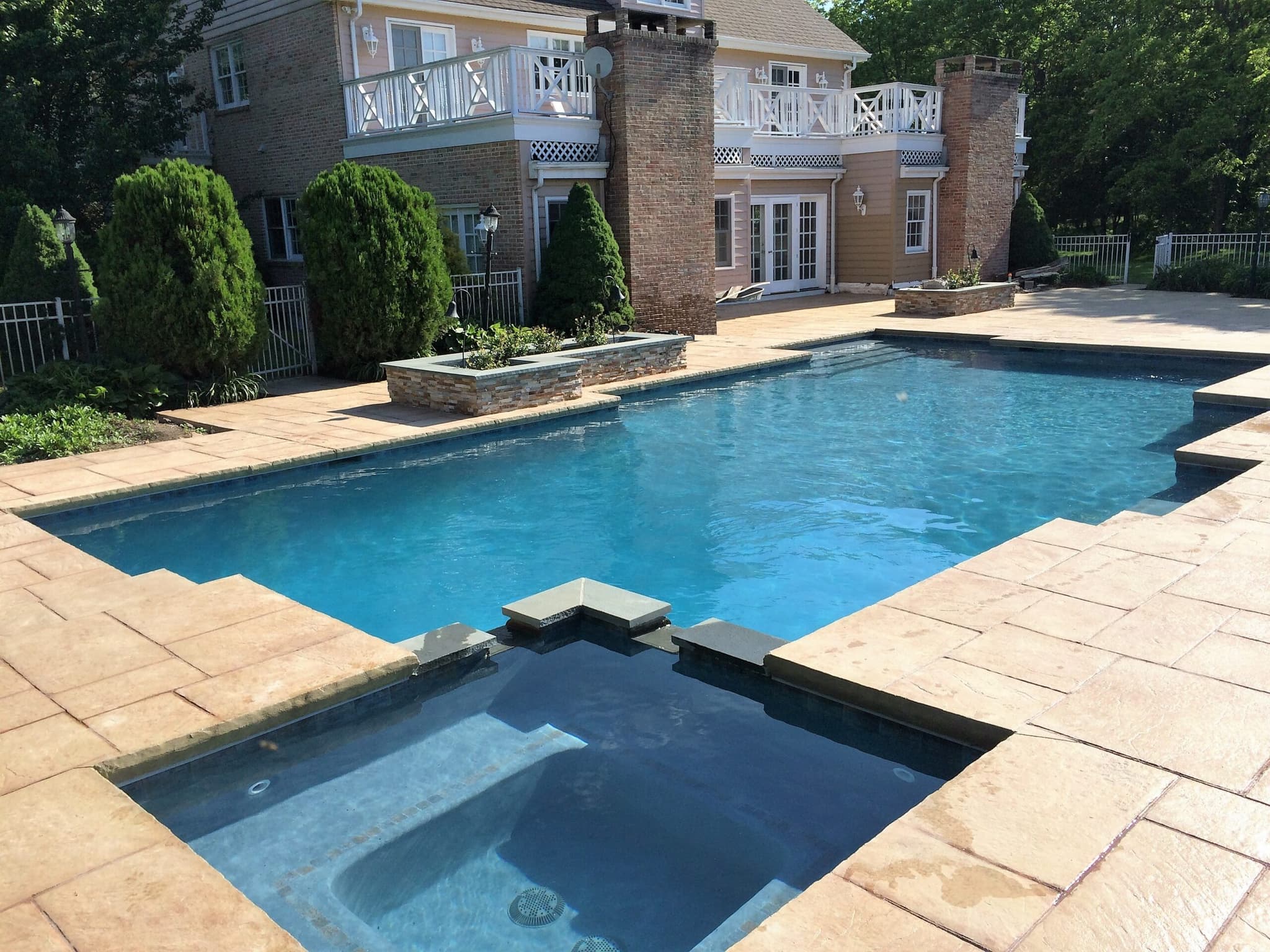 Rectangular pool with attached square spa next to brick colonial home and flagstone deck