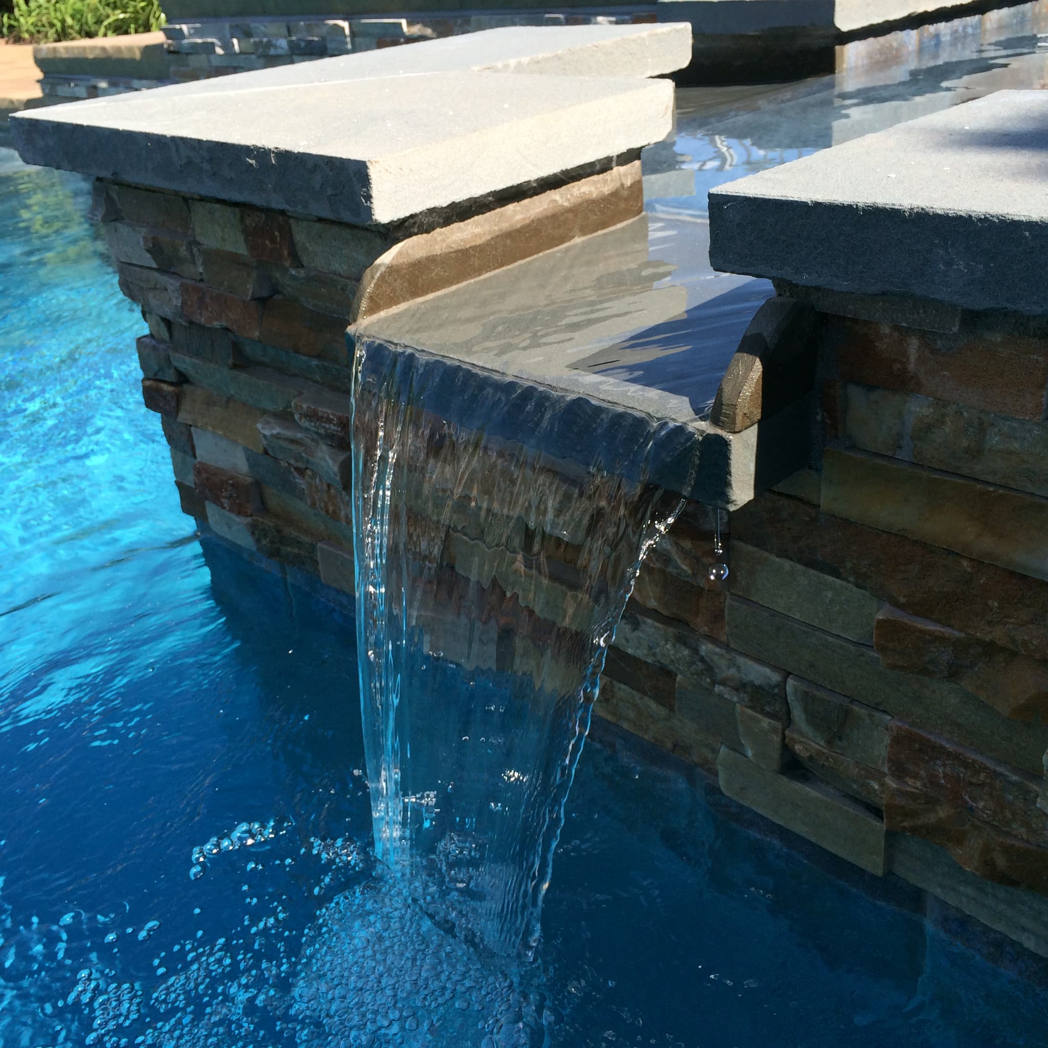 Close-up of bluestone scupper waterfall flowing into pool with pebble finish