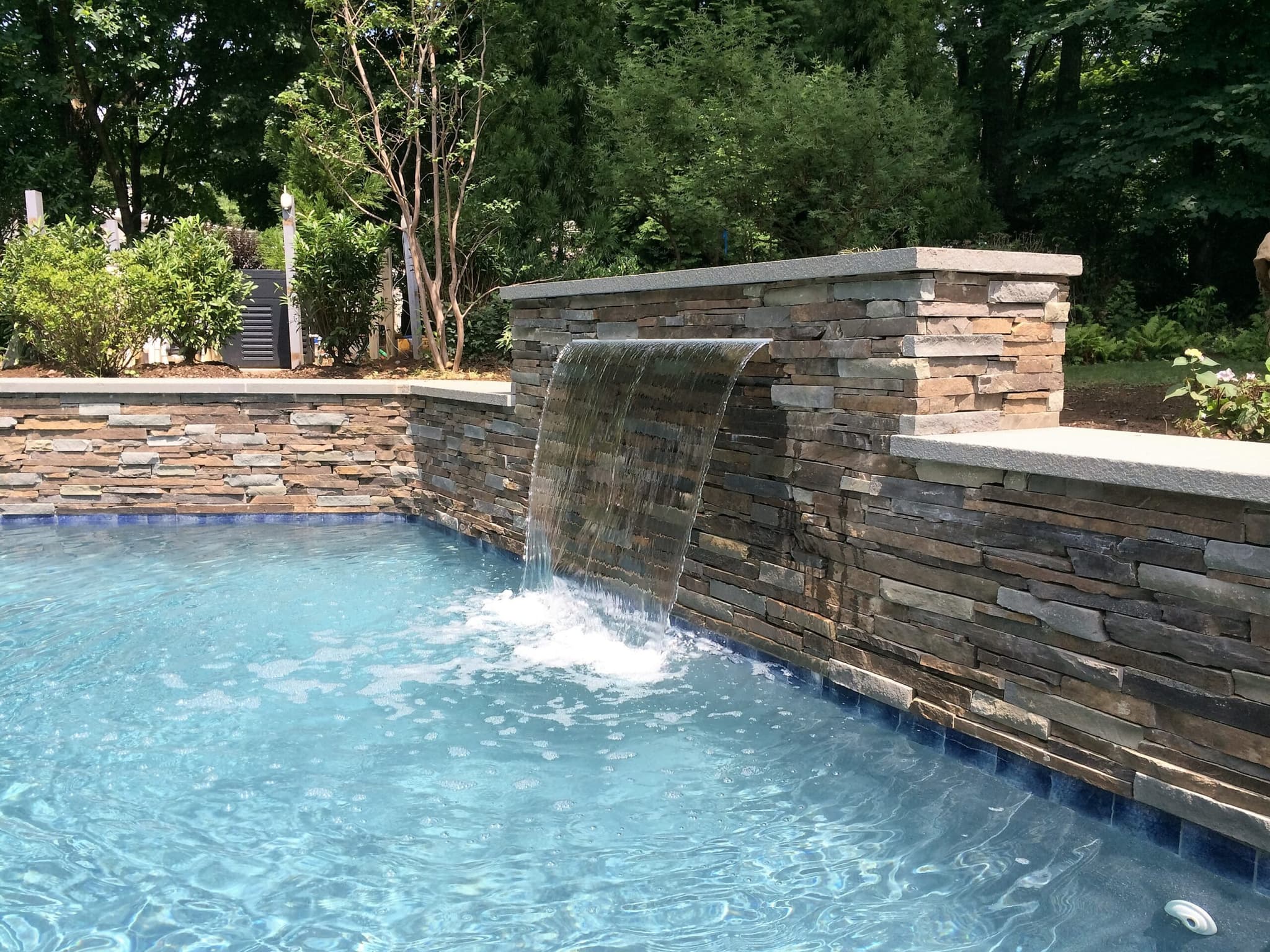 Sheer descent waterfall on stacked stone wall flowing into a swimming pool
