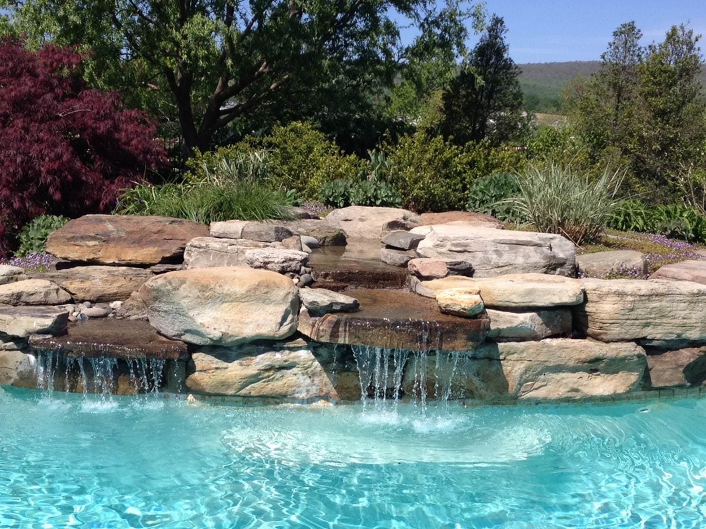 Natural boulder waterfall with twin streams pouring into pool with Japanese maple