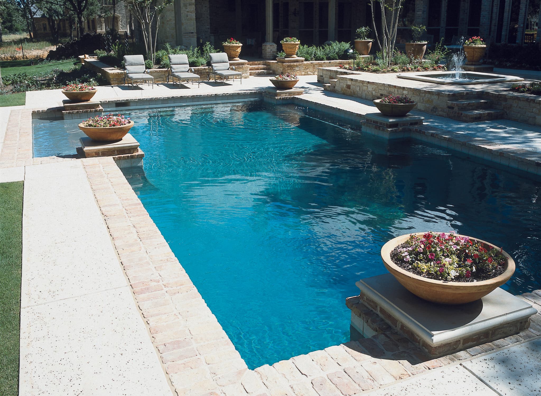 Geometric pool with raised spa, bubbler fountain, brick coping and floral planters