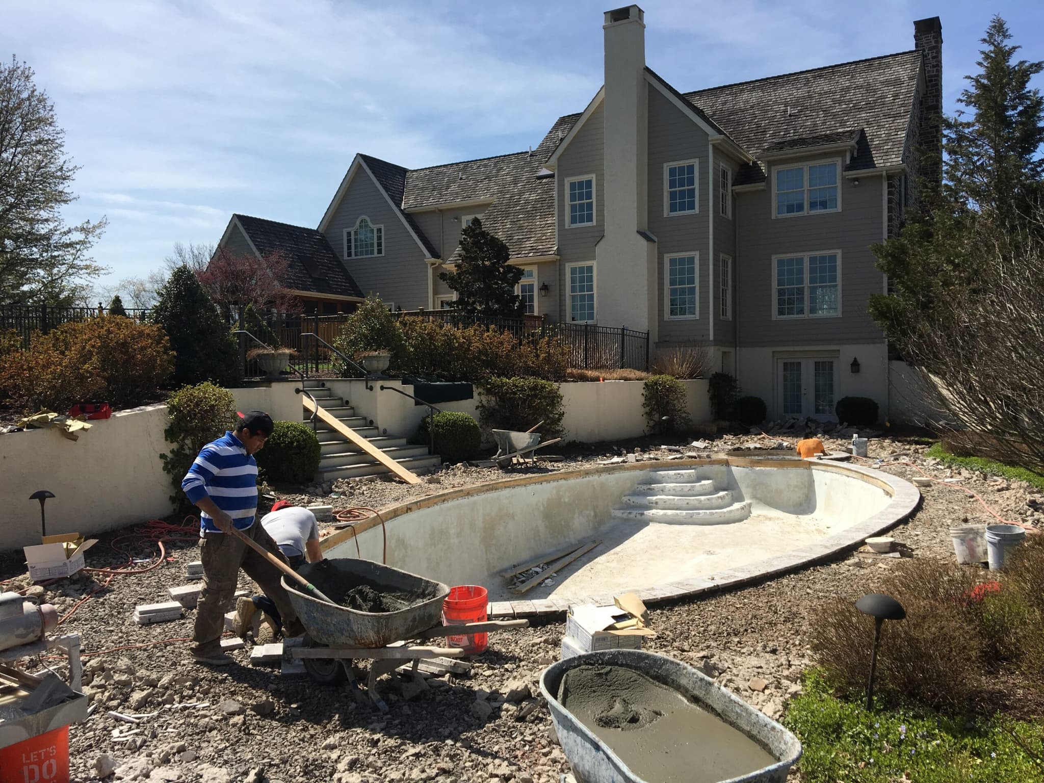 Rectangular pool gunite shell with workers laying steps at gray clapboard estate