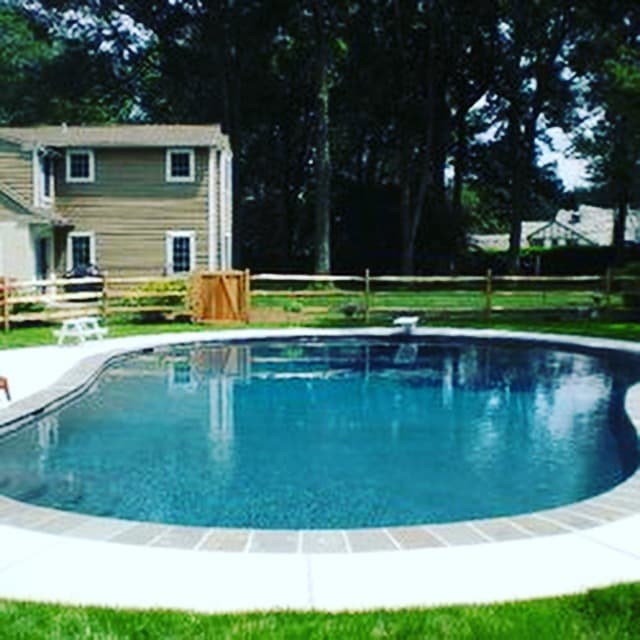 Teardrop freeform pool with stone coping behind beige clapboard home (Instagram crop)
