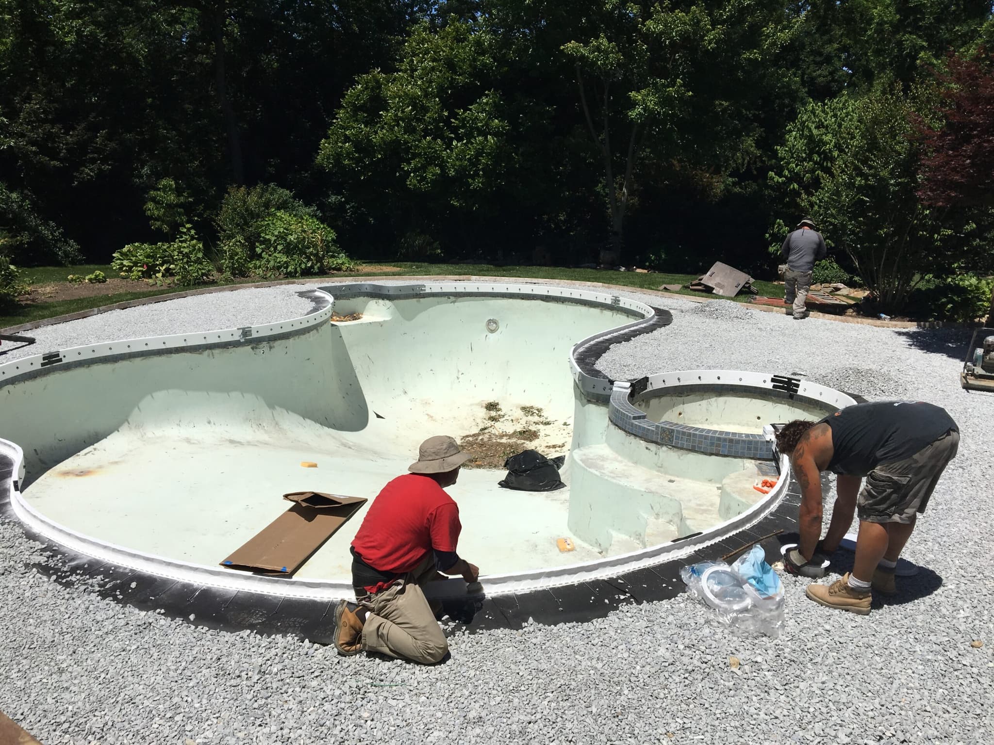 Pool gunite shell during resurfacing with two workers applying finish inside