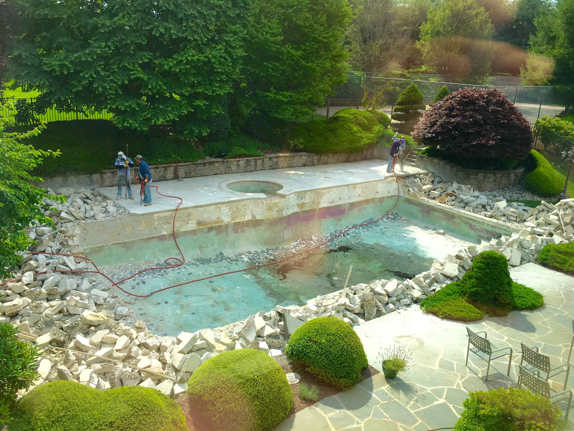 Freeform pool drained with crew repairing flagstone coping during renovation
