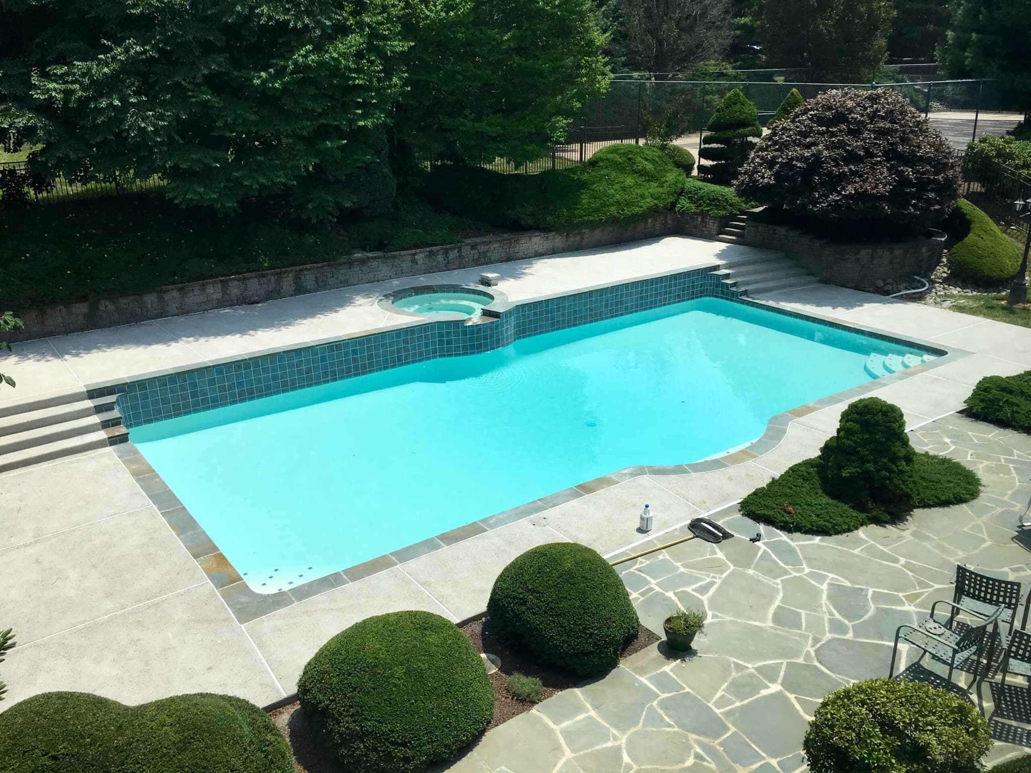Rectangular pool with raised spa, glass tile band and flagstone deck in formal garden