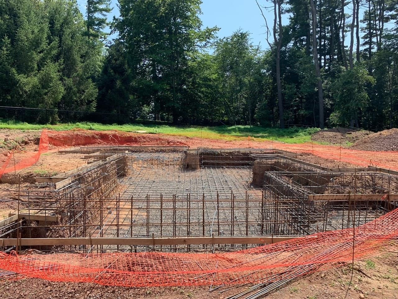 Pool construction in progress showing rebar grid and orange safety fencing before gunite