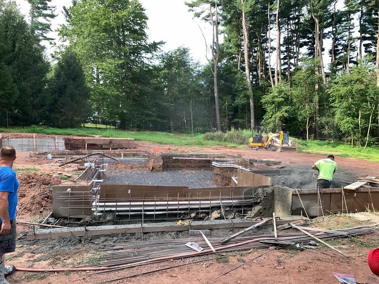 Pool excavation with rebar steel cage being tied by workers and excavator on site
