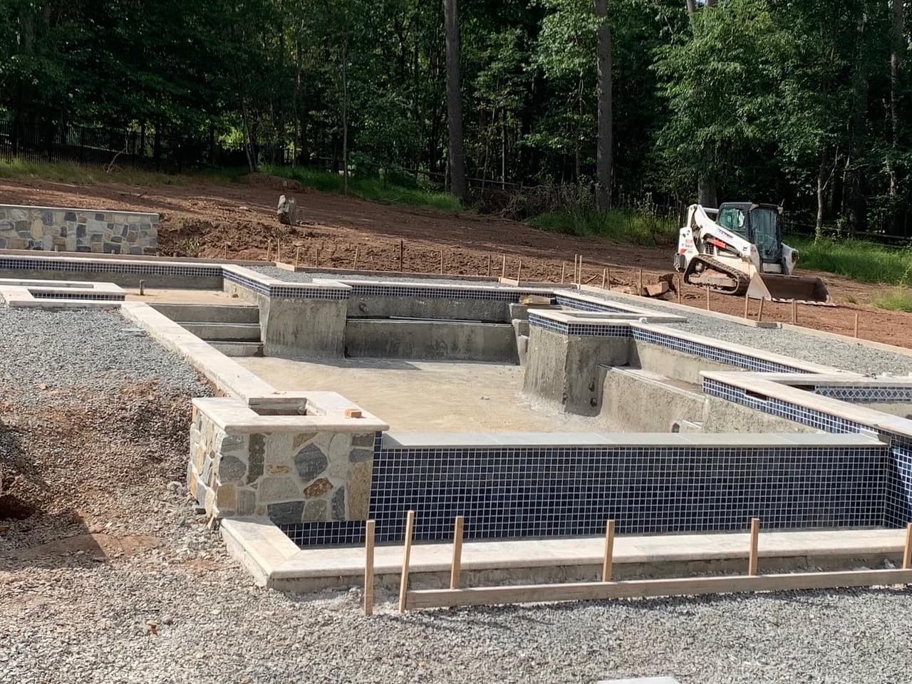 Pool gunite shell with blue waterline tile installed and skid steer on site during construction
