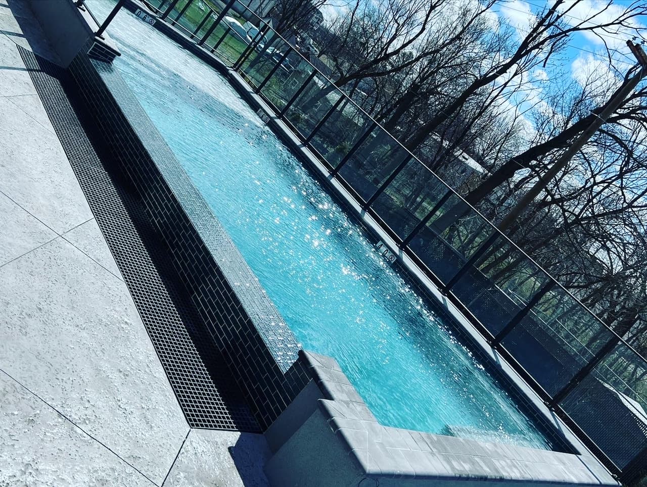 Modern lap pool with vanishing edge and dark mosaic tile against iron fence