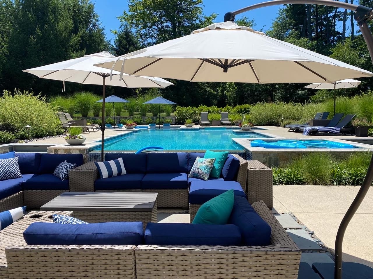 Modern rectangular pool with attached spa, navy outdoor sectional and large umbrellas on flagstone patio