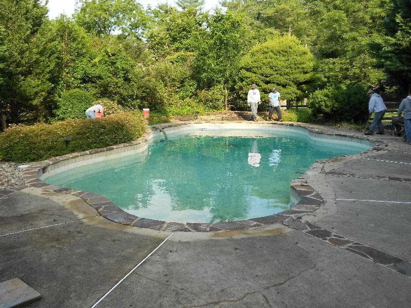 Crew applying fresh blue plaster to freeform pool during resurfacing project