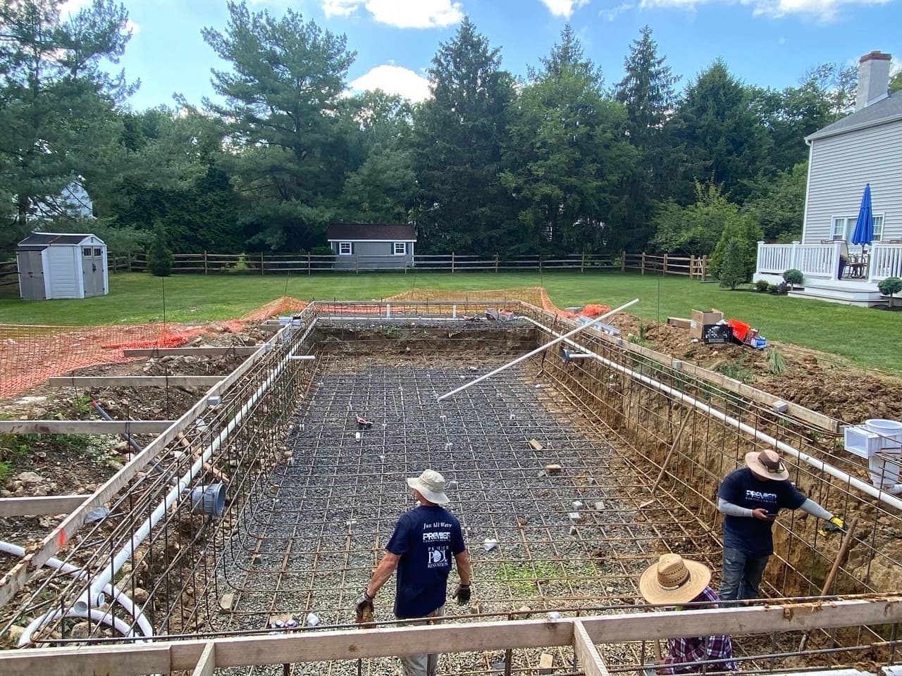 Rectangular pool gunite shell with rebar grid mid-construction at clapboard home