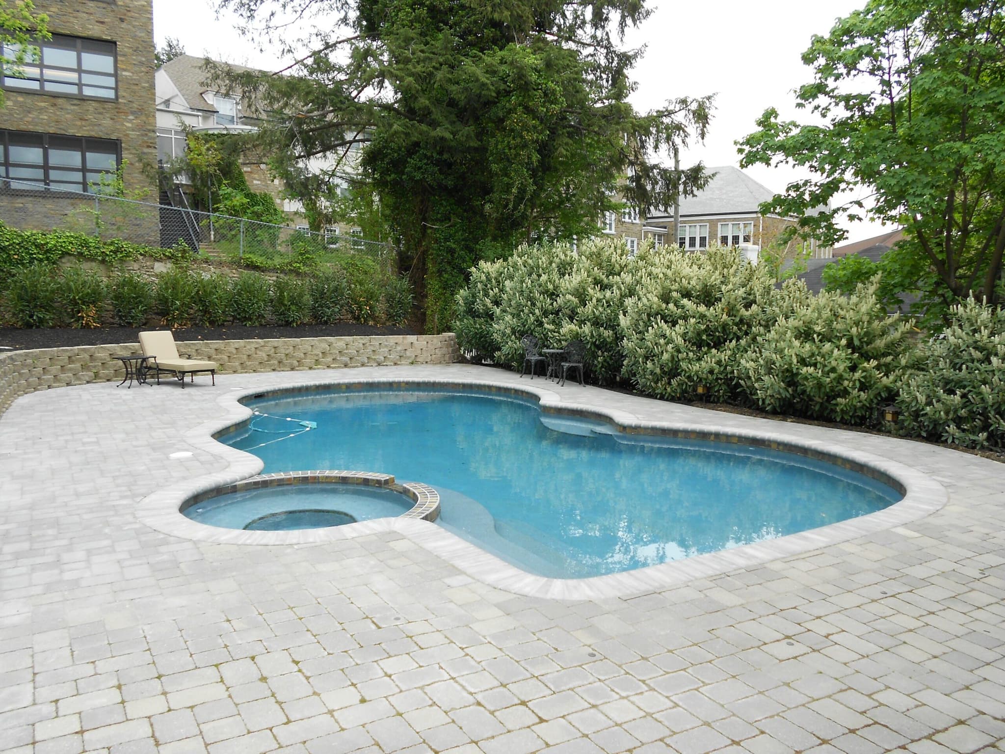 Freeform pool with attached spa and brick paver deck on urban hillside lot