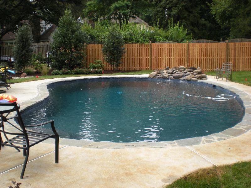 Kidney pool with French gray plaster and rock waterfall behind privacy fence