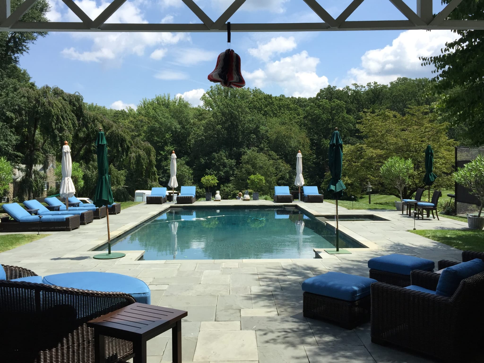 Rectangular pool viewed from pergola seating with green umbrellas in hilly wooded yard