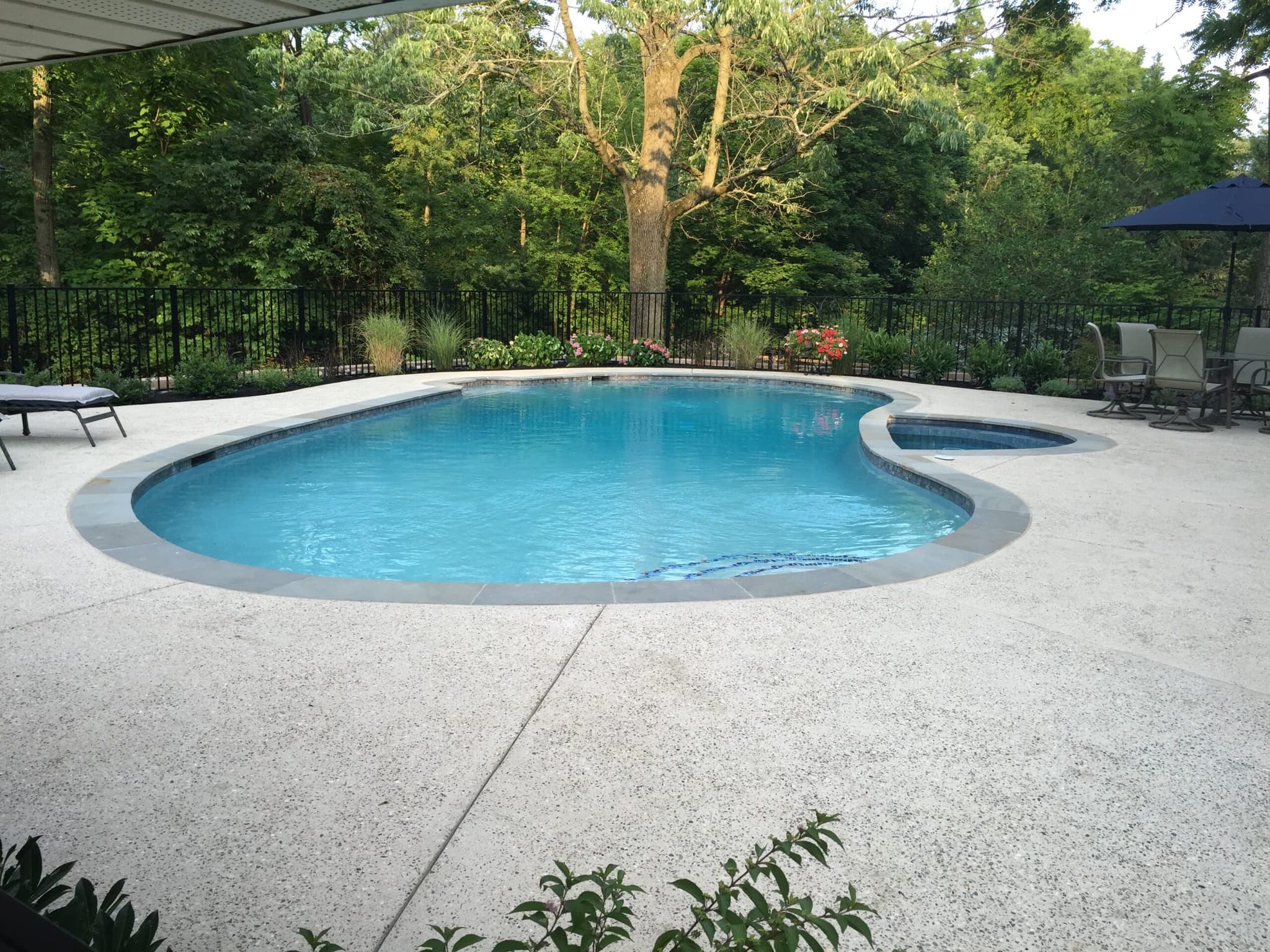 Freeform pool with attached round spa and exposed-aggregate deck in wooded backyard