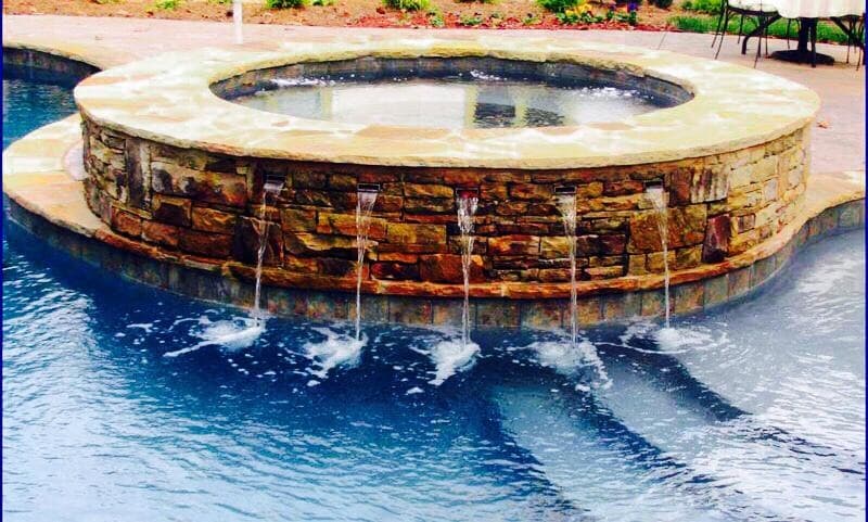Round raised stone spa with five sheer-descent waterfalls spilling into pool