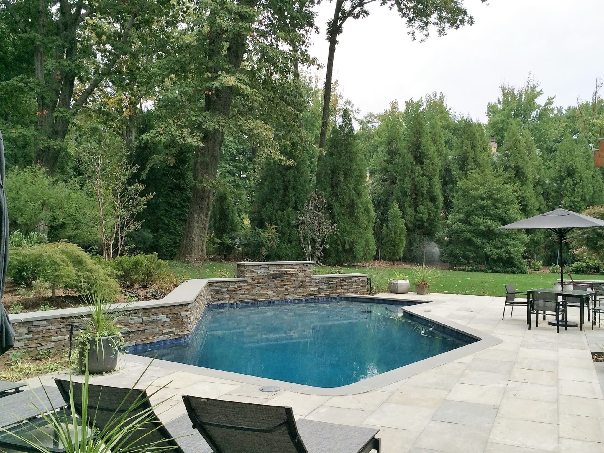 Rectangular pool with raised stone spa and waterfalls on travertine deck under tall pines
