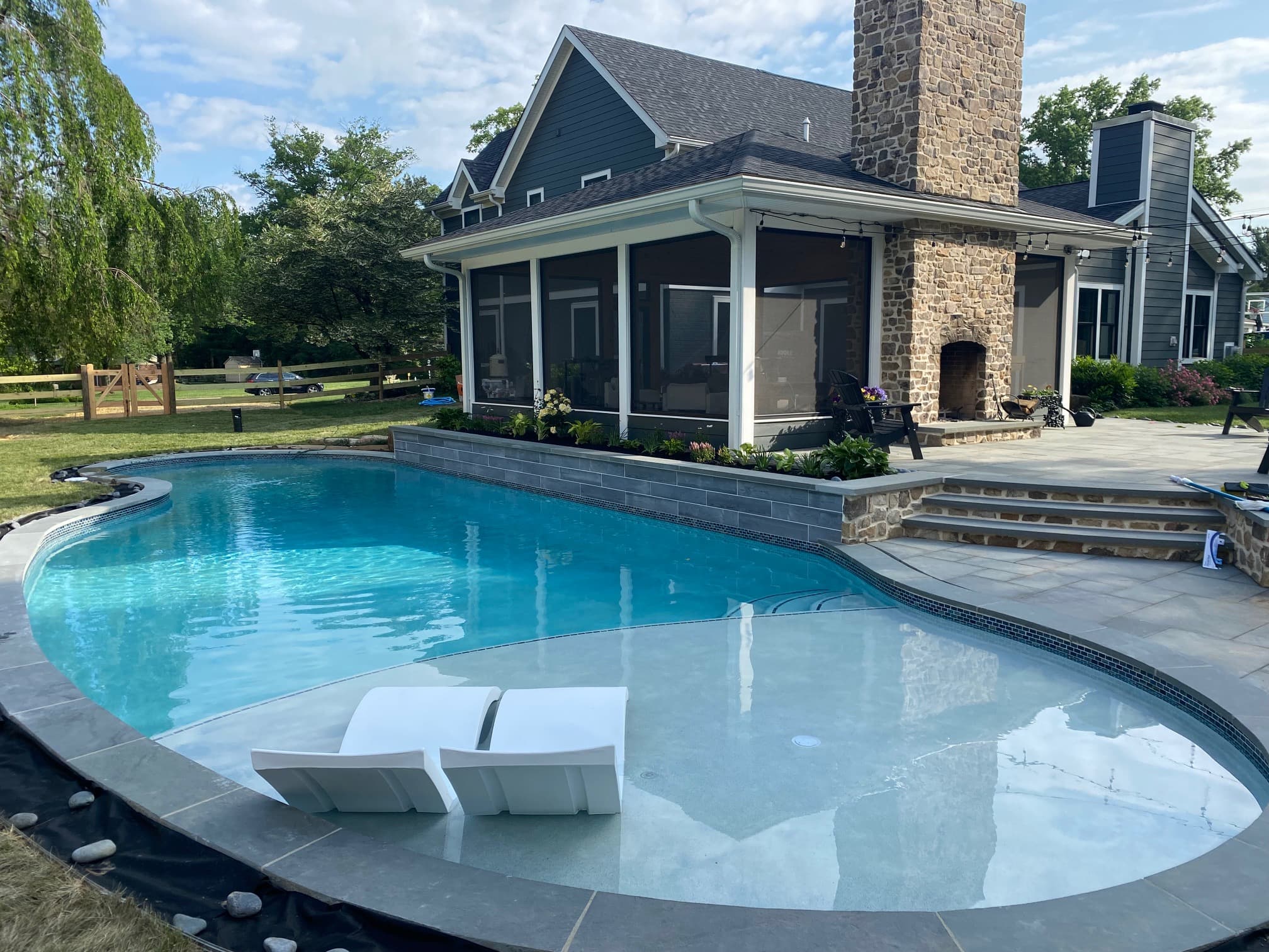 Freeform pool with tanning ledge, in-pool lounger and stone-chimney screened porch home behind