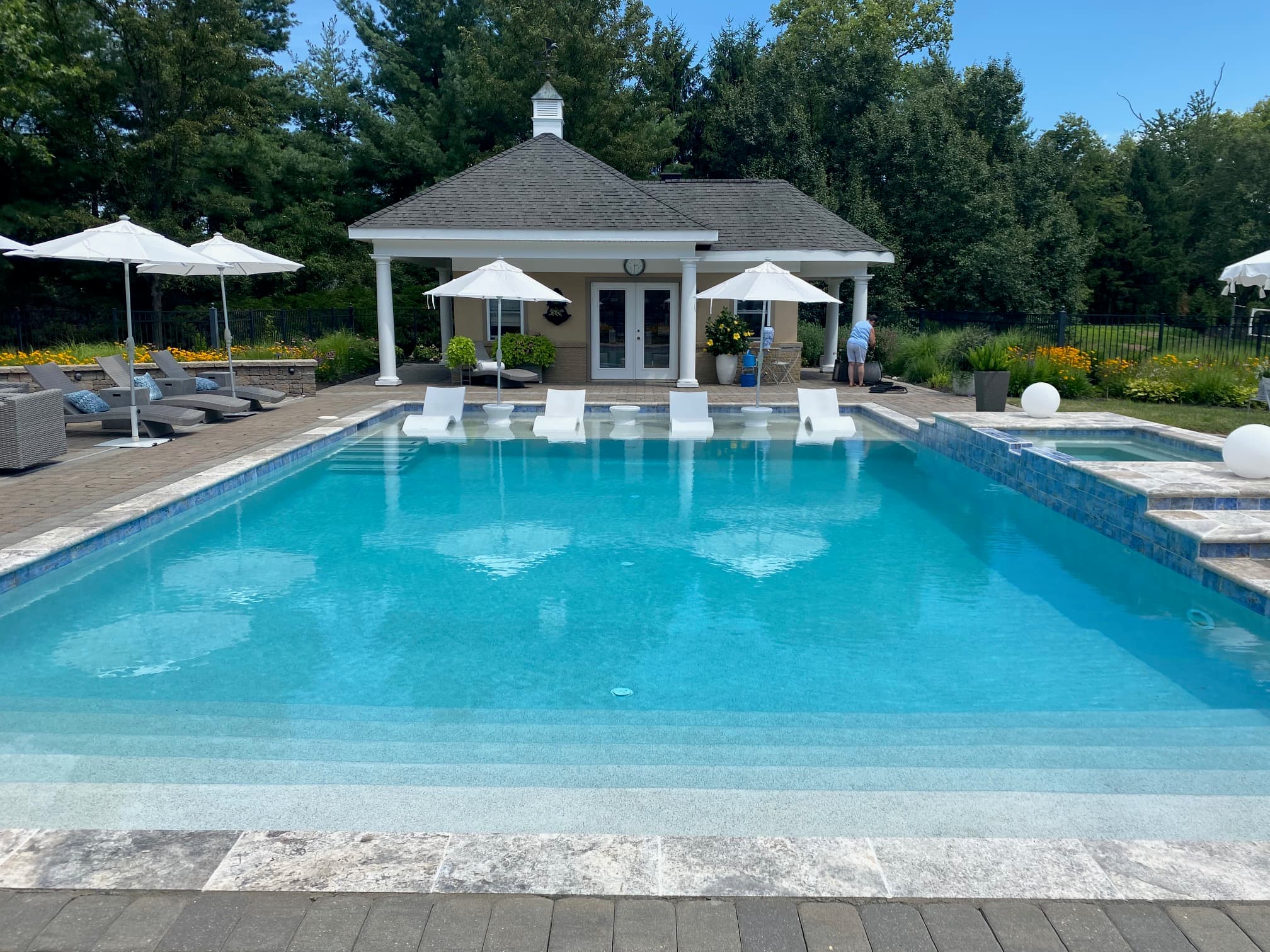 Rectangular pool with attached spa and ledge loungers in front of white pool house