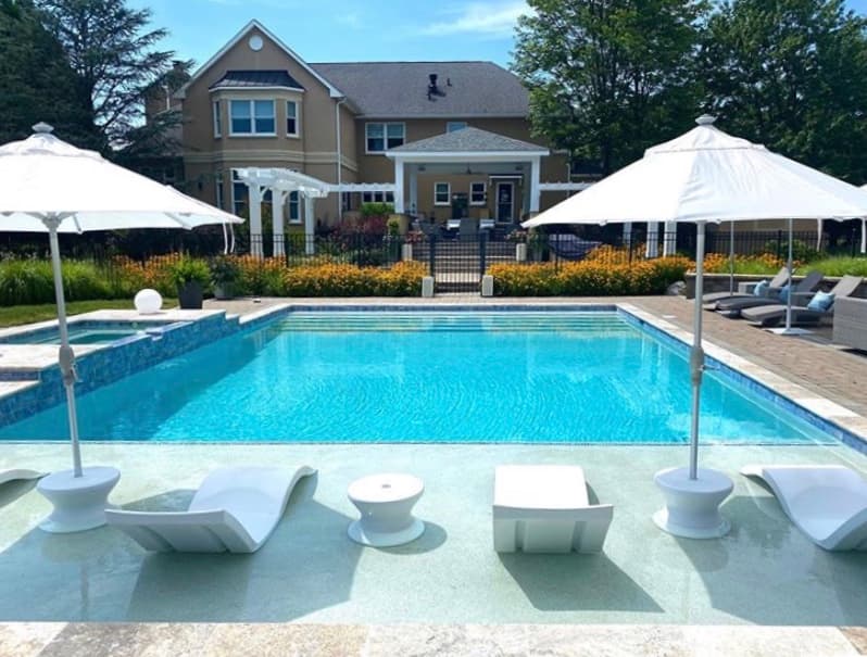 Modern rectangular pool with in-pool loungers, white umbrellas and attached spa at a formal estate — Premier Pool Renovations