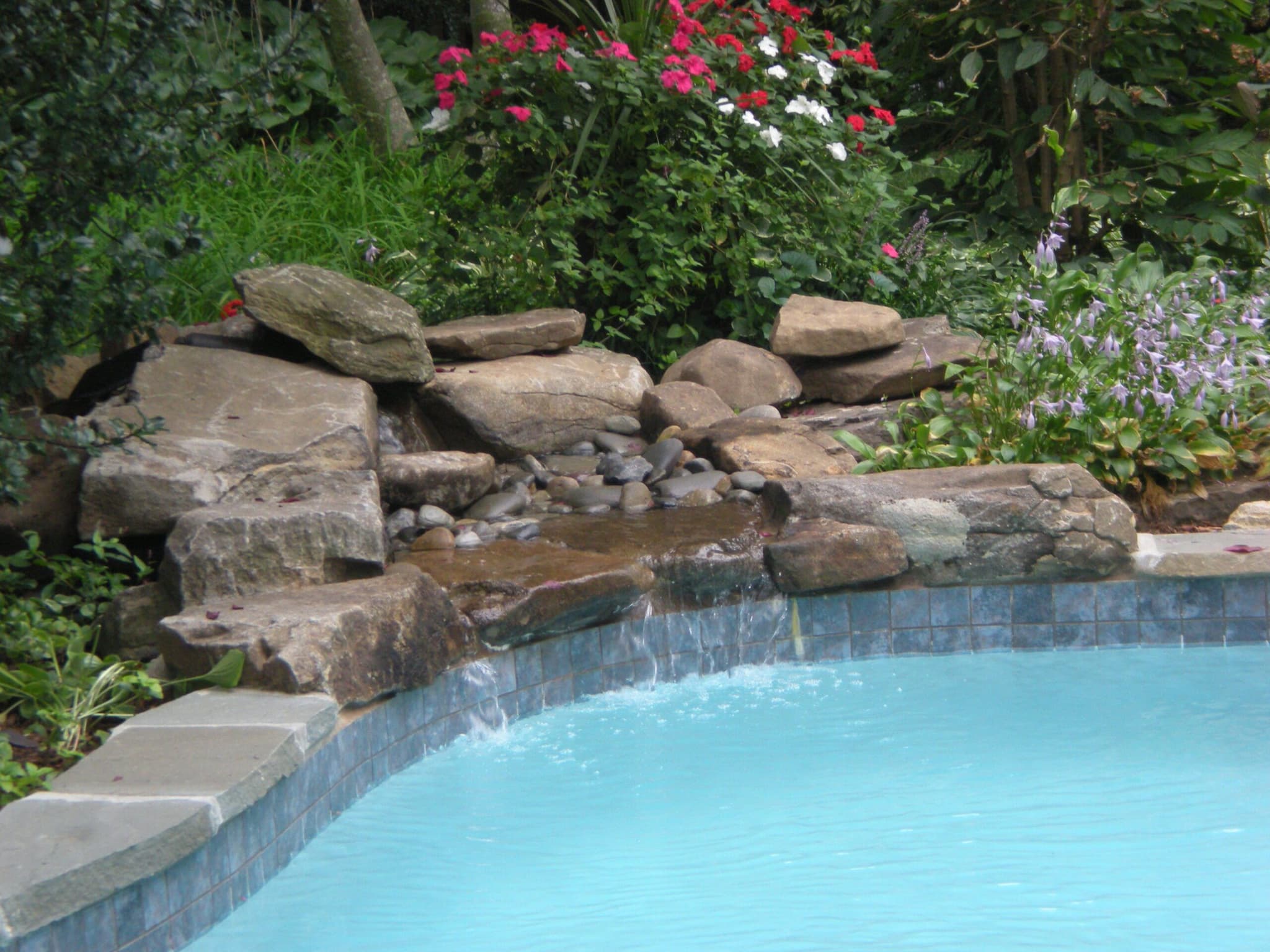 Natural stone waterfall feature spilling into pool with blue tile and impatiens border
