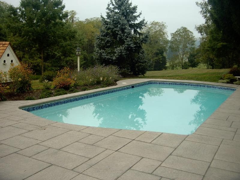 Lazy-L pool with blue waterline tile and stamped concrete deck on hillside lot