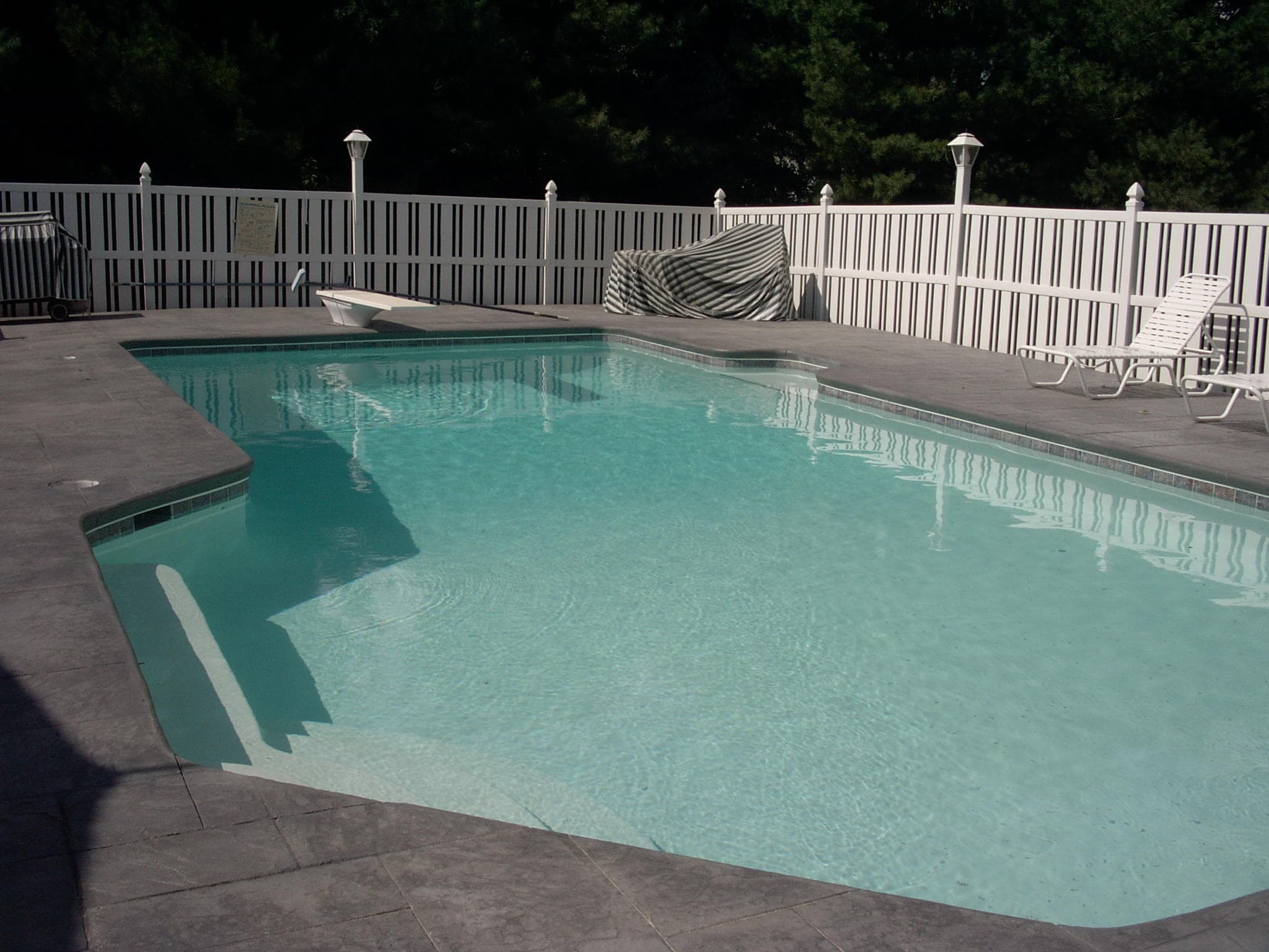 Rectangular pool after renovation with white vinyl fence and stamped concrete deck