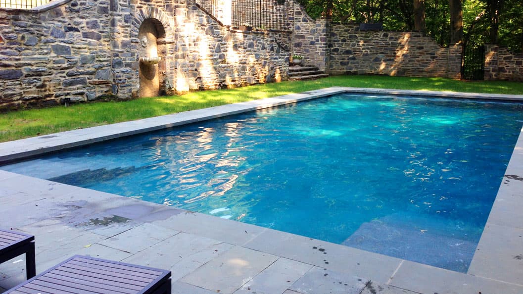 Rectangular pool with bluestone coping framed by historic stone wall and arched fountain niche — Premier Pool Renovations
