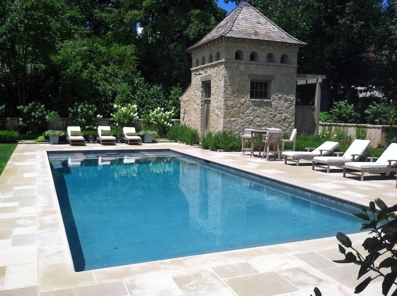 Rectangular pool with bluestone deck and stone pool-house turret on landscaped estate