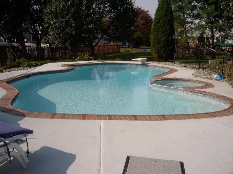 Lazy-L pool with red brick coping and attached spa in suburban backyard