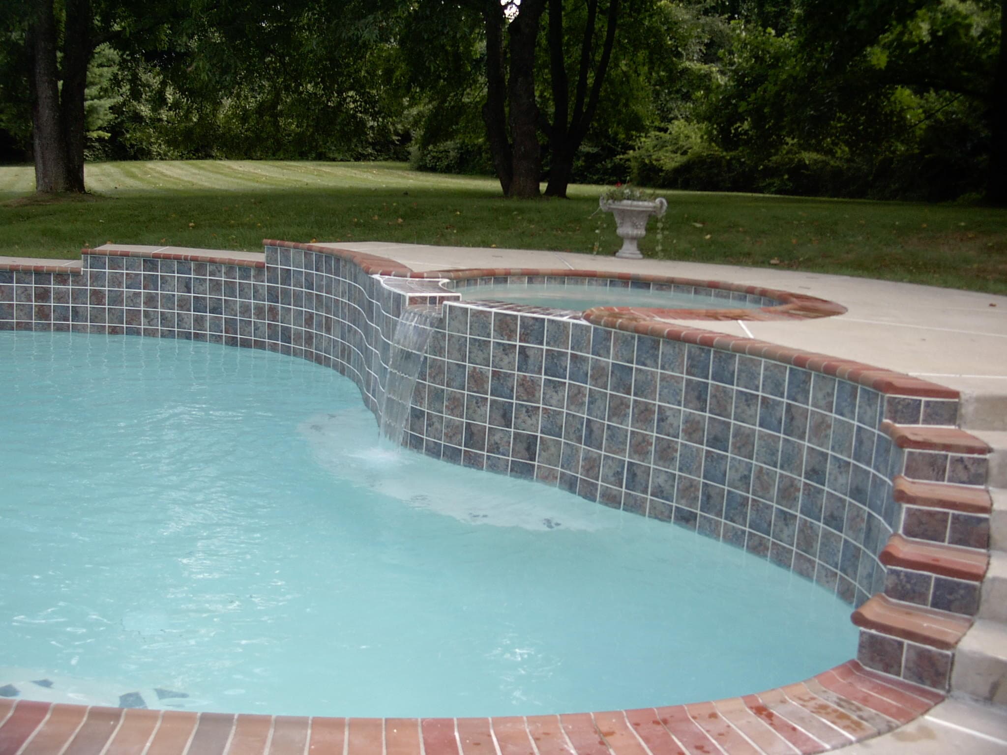 Close-up of mosaic-tile dam wall with sheer descent waterfall and brick coping