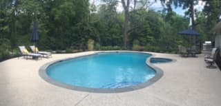 Freeform pool with blue umbrellas in wooded backyard (low-resolution thumbnail)