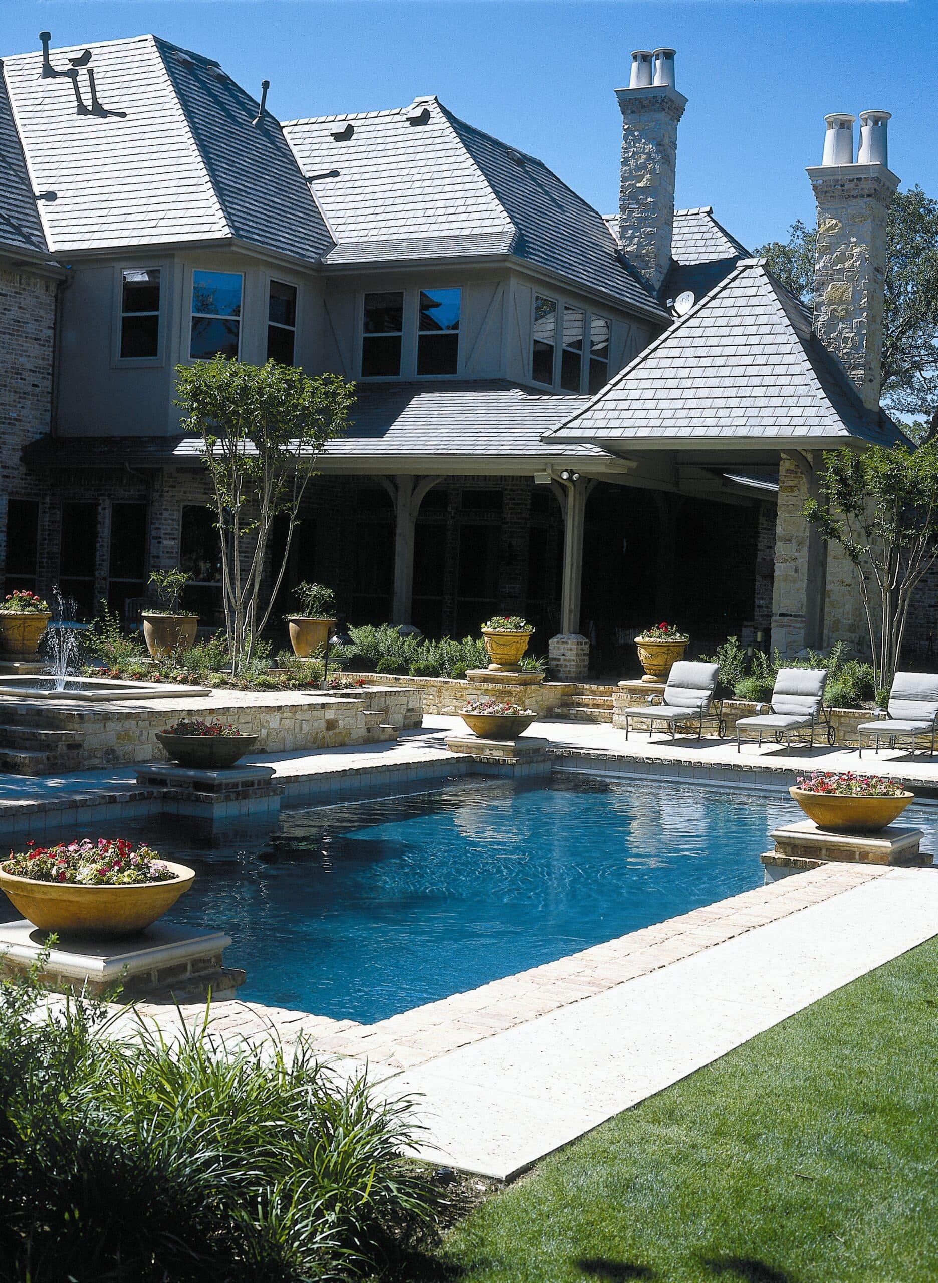 Formal rectangular pool with raised planters and chimneys behind ornate estate home