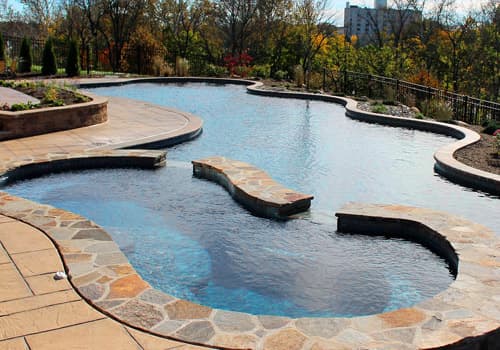Freeform pool with raised flagstone planters and autumn hillside backdrop