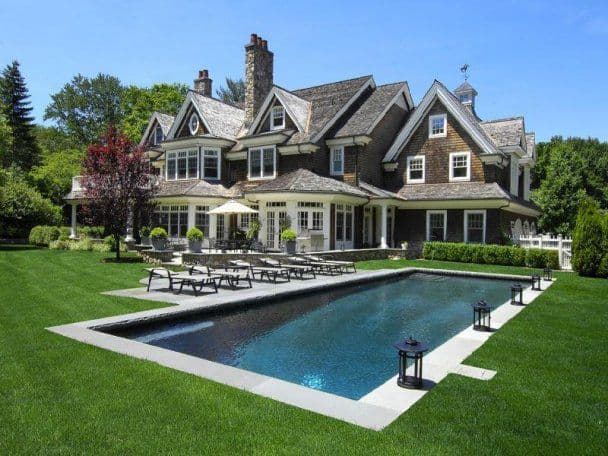 Long lap pool with lanterns alongside shingle-style estate home and manicured lawn