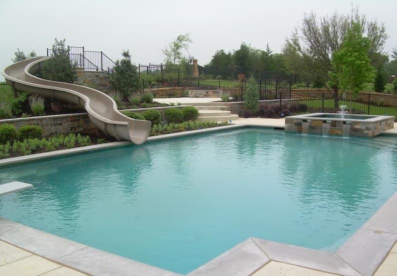 Rectangular pool with stone-walled water slide and raised square spa in fenced estate yard