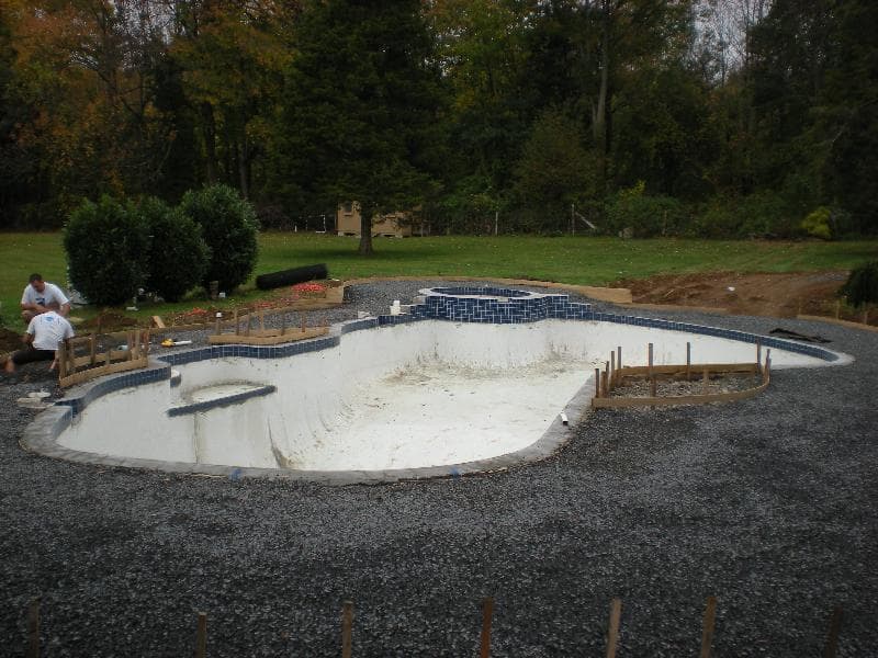 Freeform pool under construction with new blue tile band and fresh plaster before water fill