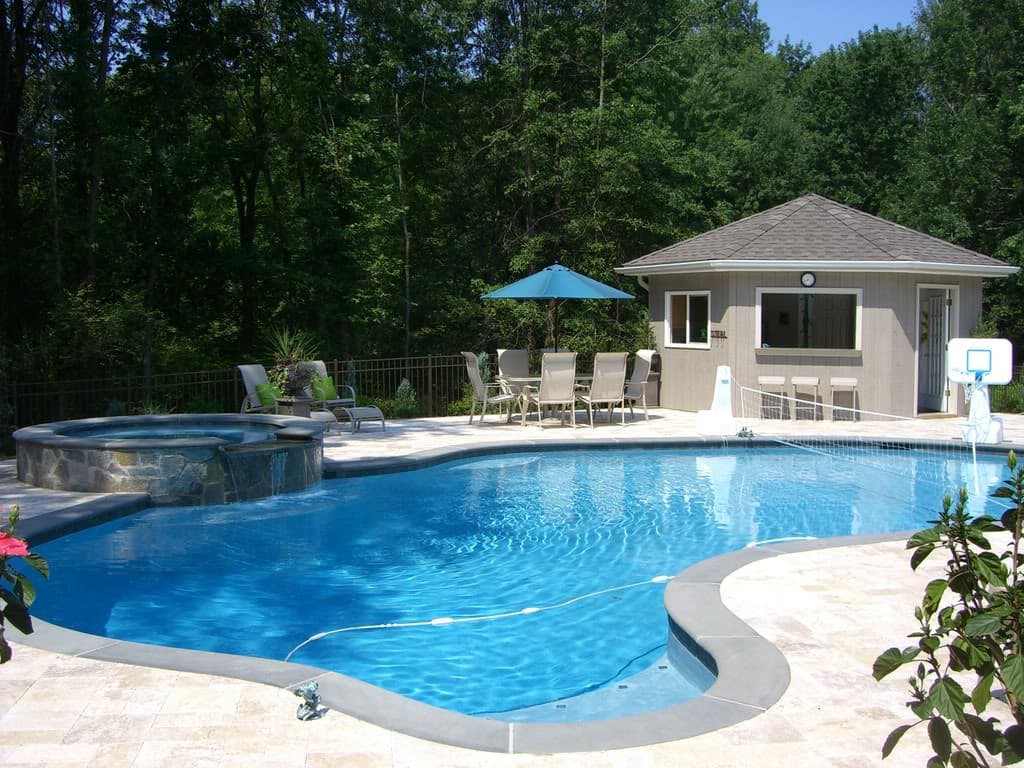 Freeform pool with raised stone spa, travertine deck and pool house — Premier Pool Renovations