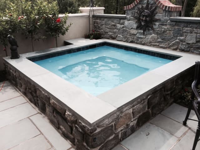 Square stone spa with bluestone coping and sun-face wall art — Premier Pool Renovations